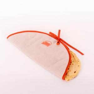 Porta piadina in tessuto beige con bordo arancione e logo "Il Panaro", contenente una piadina parzialmente visibile.