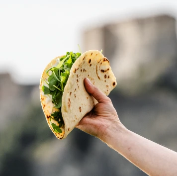 Una mano che tiene una piadina farcita con rucola, con un castello sullo sfondo.